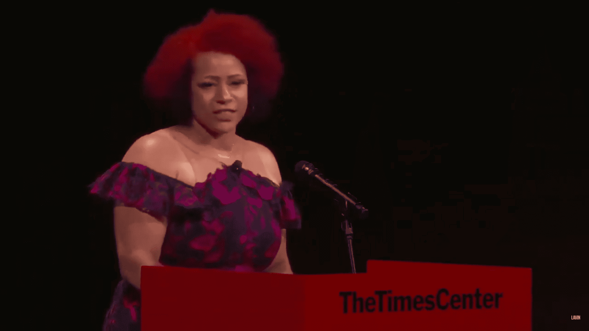 Nikole Hannah-Jones, a Black woman with curly red hair, speaking at a podium