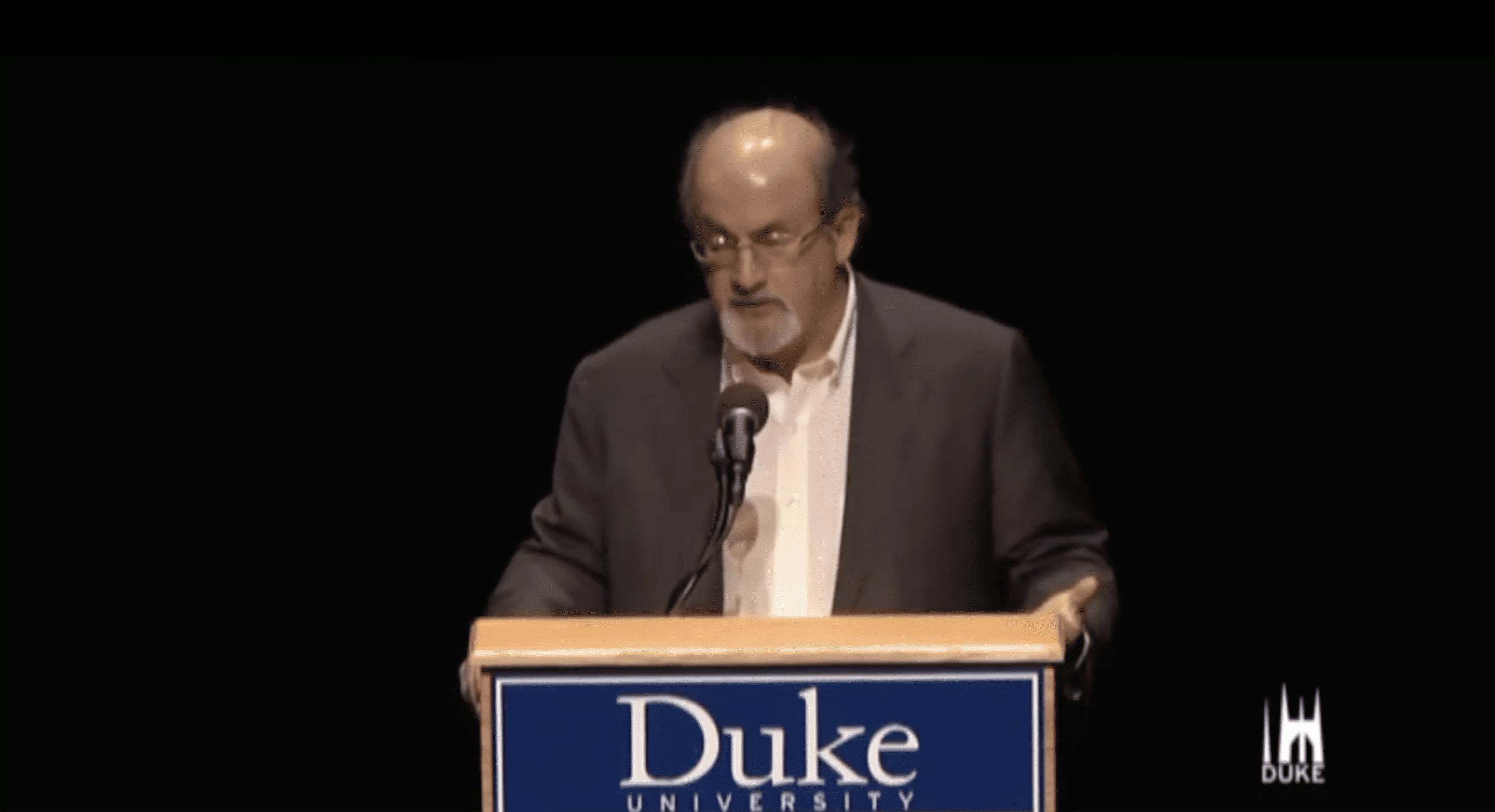 Salman Rushdie, a brown-skinned man, gives a talk at Duke University.