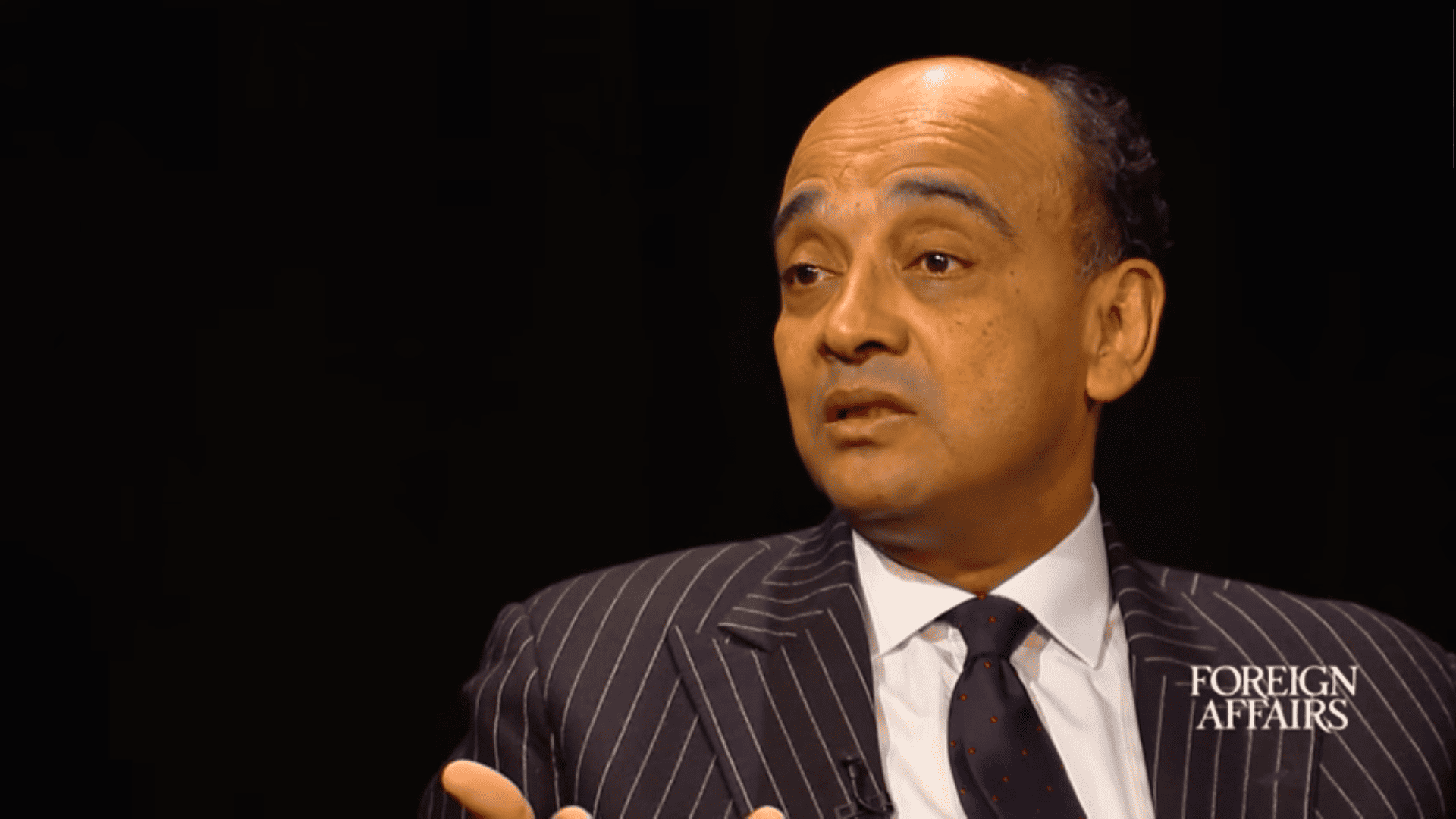Kwame Anthony Appiah, a dark-skinned man in a suit, speaking with an interviewer.