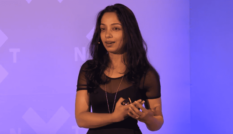 Radhika Dirks, a brown-skinned woman with dark hair, gives a talk onstage.