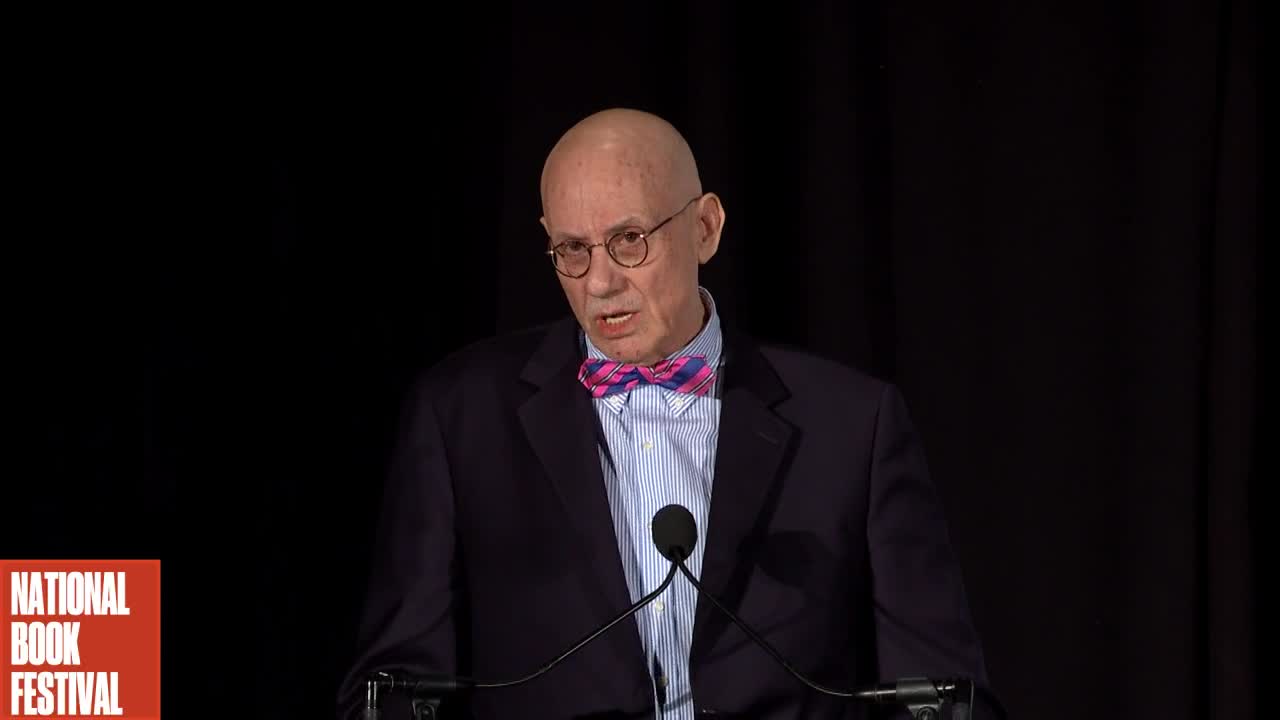 James Ellroy, a light-skinned man with glasses, giving a talk.