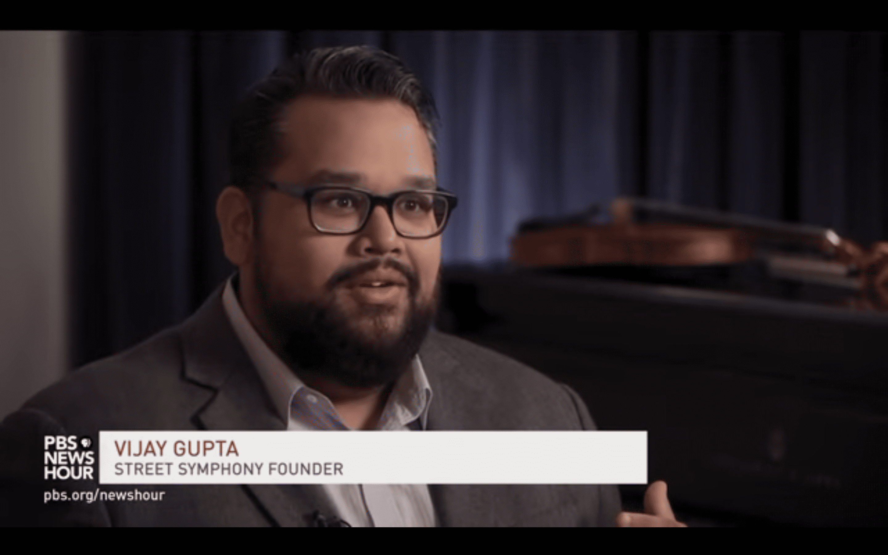 Vijay Gupta, a brown-skinned man, giving an interview on PBS.