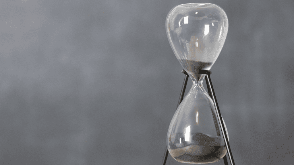 An hourglass filled with grey sand against a grey background.