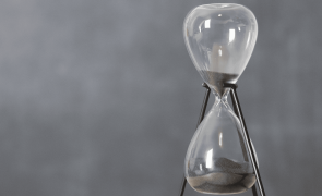 An hourglass filled with grey sand against a grey background.